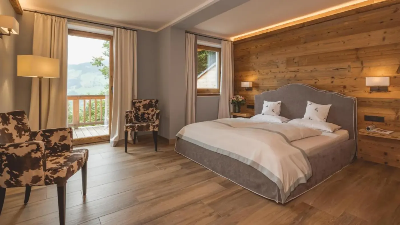 Double bedroom with a timber feature wall and balcony doors at Almlodge Westendorf in Westendorf, Austria.