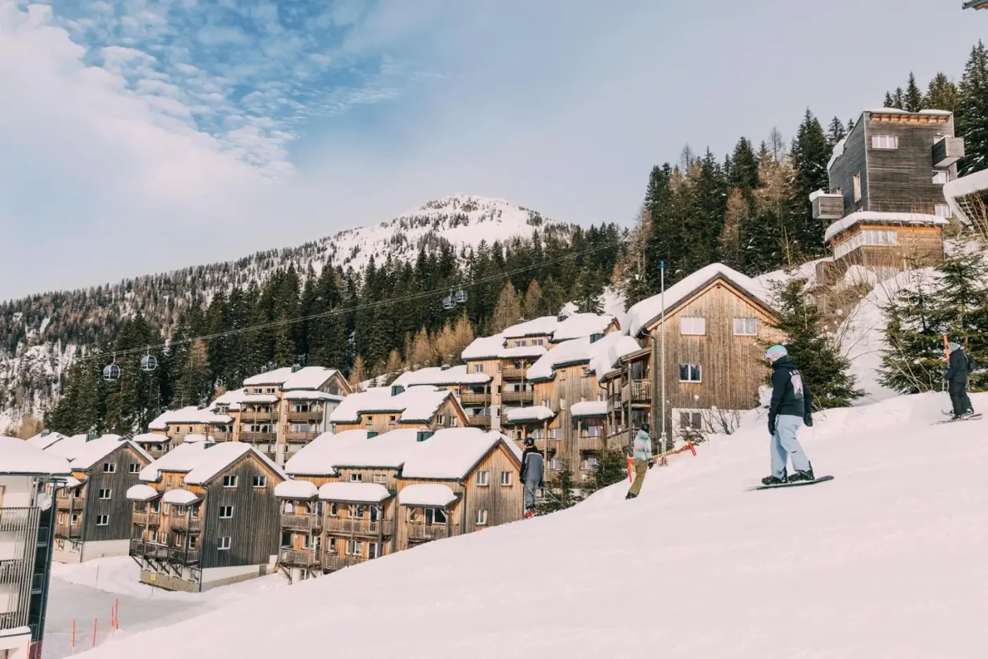 Snow-covered timber chalet resort beside alpine ski slopes at Almresort Gartnerkofel Nassfeld in Hermagor, Austria.