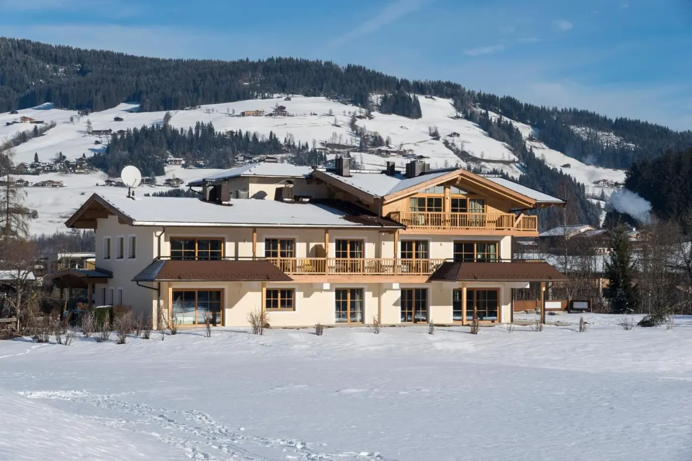 Alpine chalet exterior with timber balconies and a snow-covered lawn at Alpen Chalet Dorfwies in Kirchberg in Tirol, Austria.