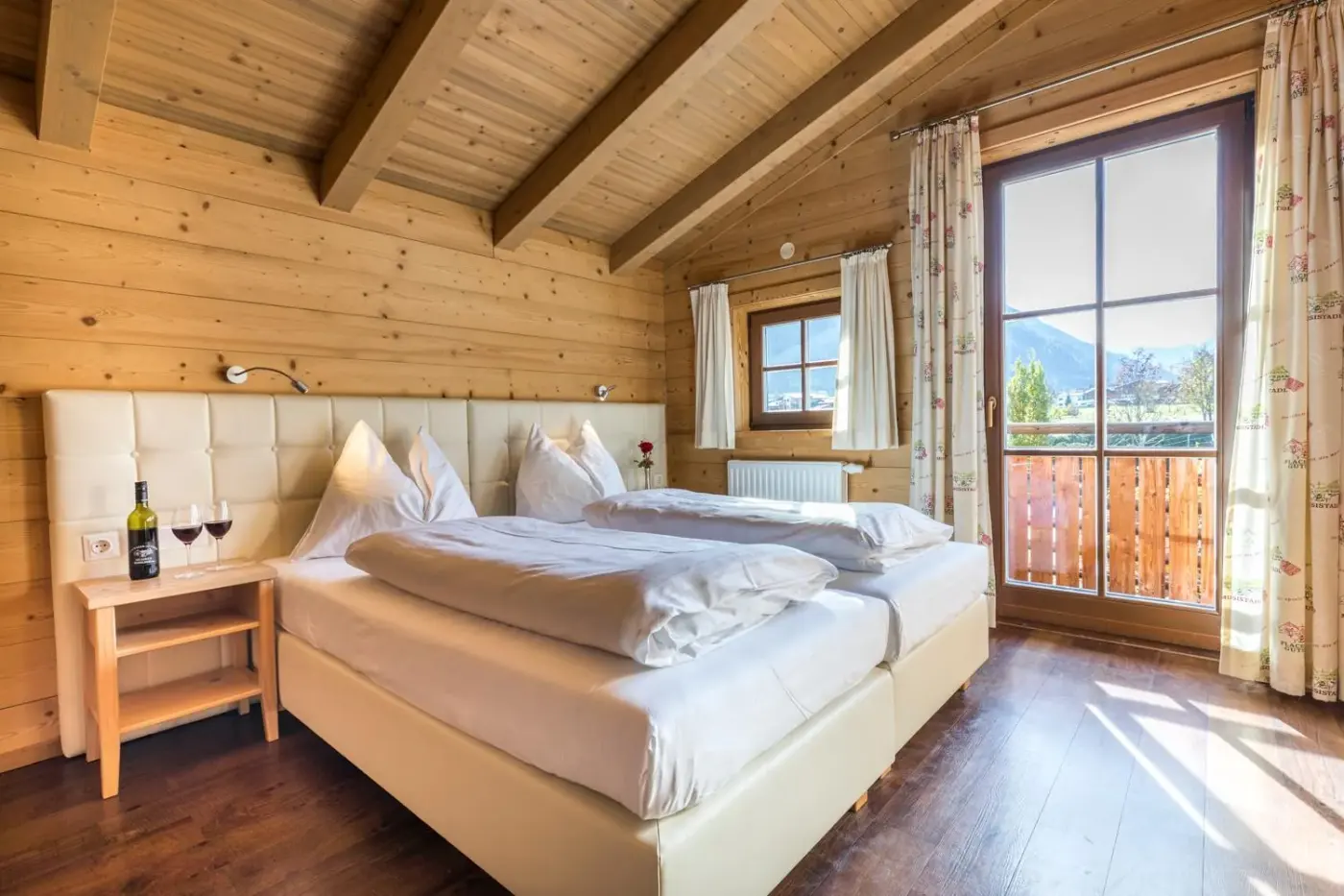 Double bedroom with exposed timber beams and balcony doors at Alpenchalets Flachauer Gutshof in Flachau, Austria.