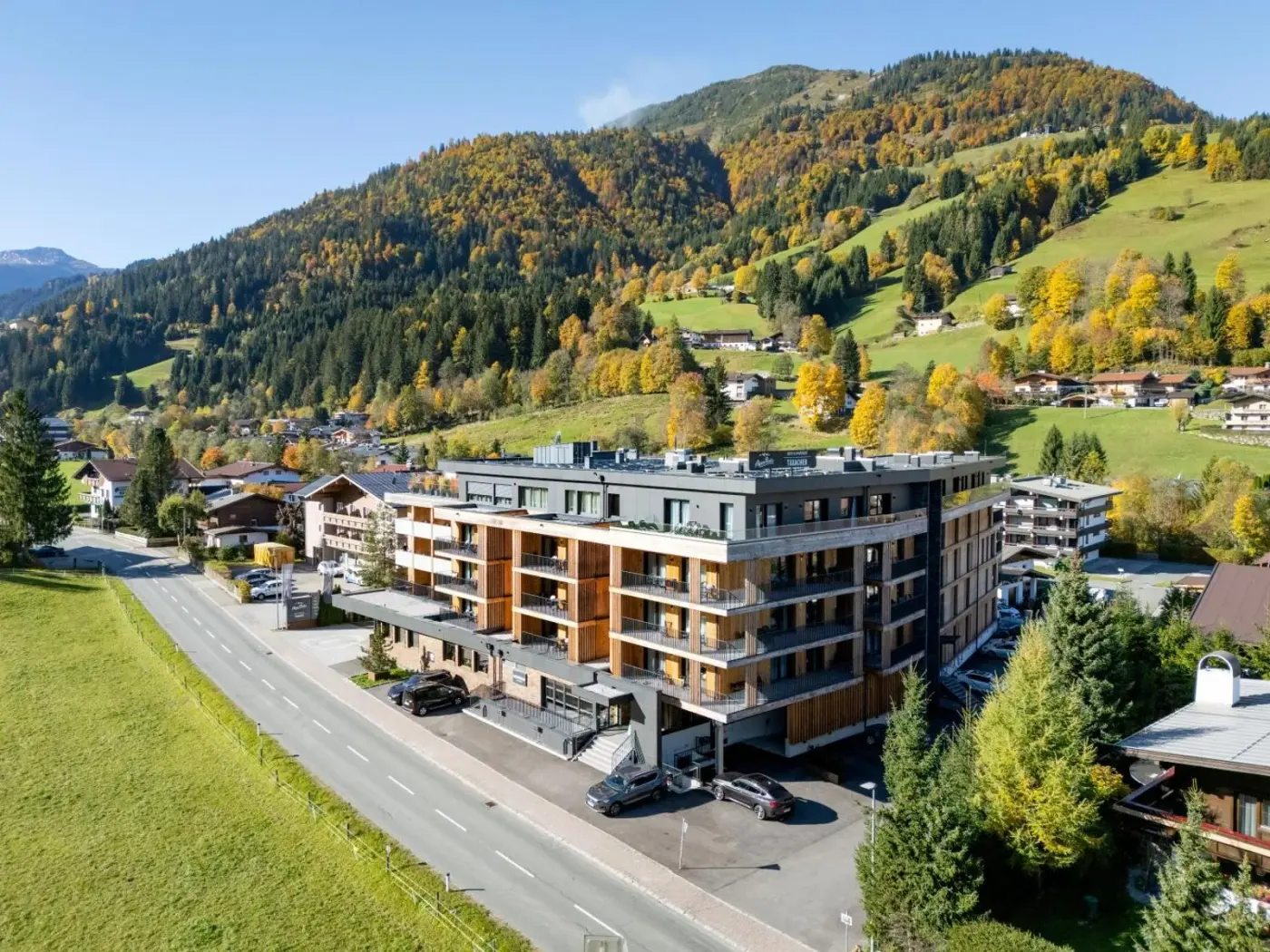 Hotel exterior with balconies beneath a hillside in autumn colours at AlpenParks Hotel and Apartment Taxacher in Kirchberg in Tirol, Austria.