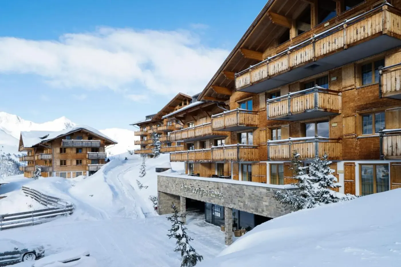 Alpine lodges with timber balconies beside a snow-covered path at AlpinLodges Kühtai in Kühtai, Austria.