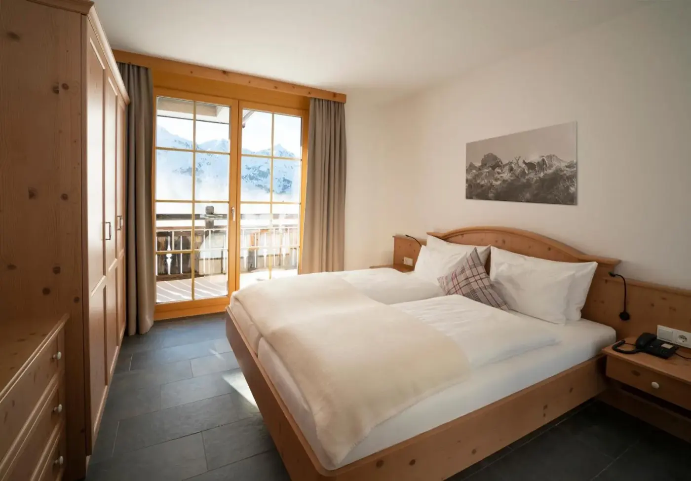 Double bedroom with timber furniture and balcony doors at AlpinLodges Kühtai in Kühtai, Austria.
