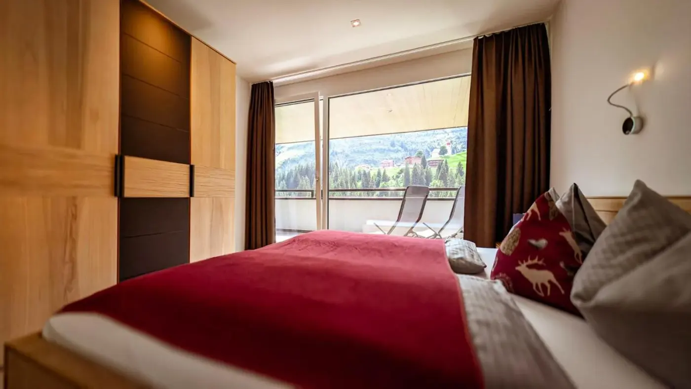 Double bedroom with red bedding and balcony doors at Aparthotel Alpinresort Damüls in Damüls, Austria.