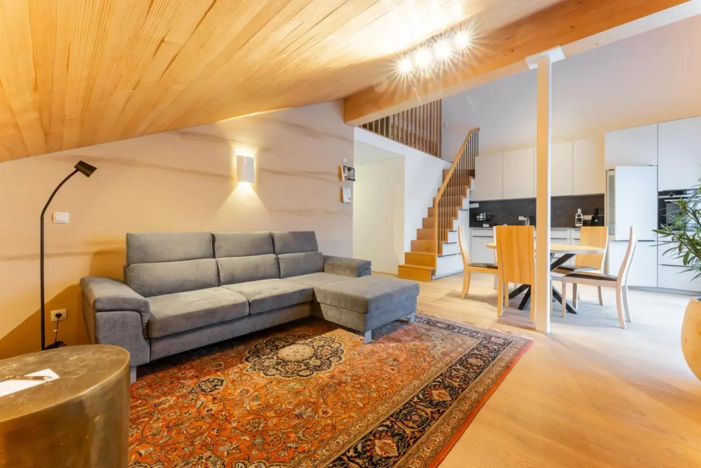 Loft living and dining room with a grey sofa and timber ceiling at Aparthotel Alpinresort Damüls in Damüls, Austria.