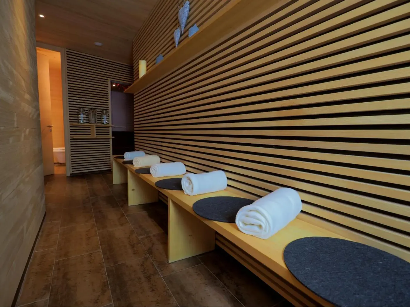 Wellness relaxation room with timber slats, wooden benches and folded towels at Aparthotel Alpinresort Damüls in Damüls, Austria.