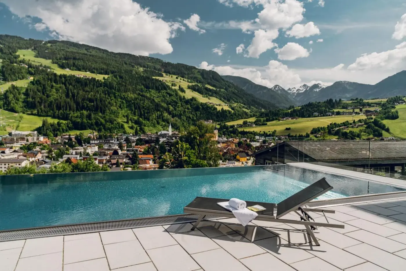 Outdoor pool and loungers overlooking a green valley and mountain peaks at Apartmentresort MyLodge in Schladming, Austria.
