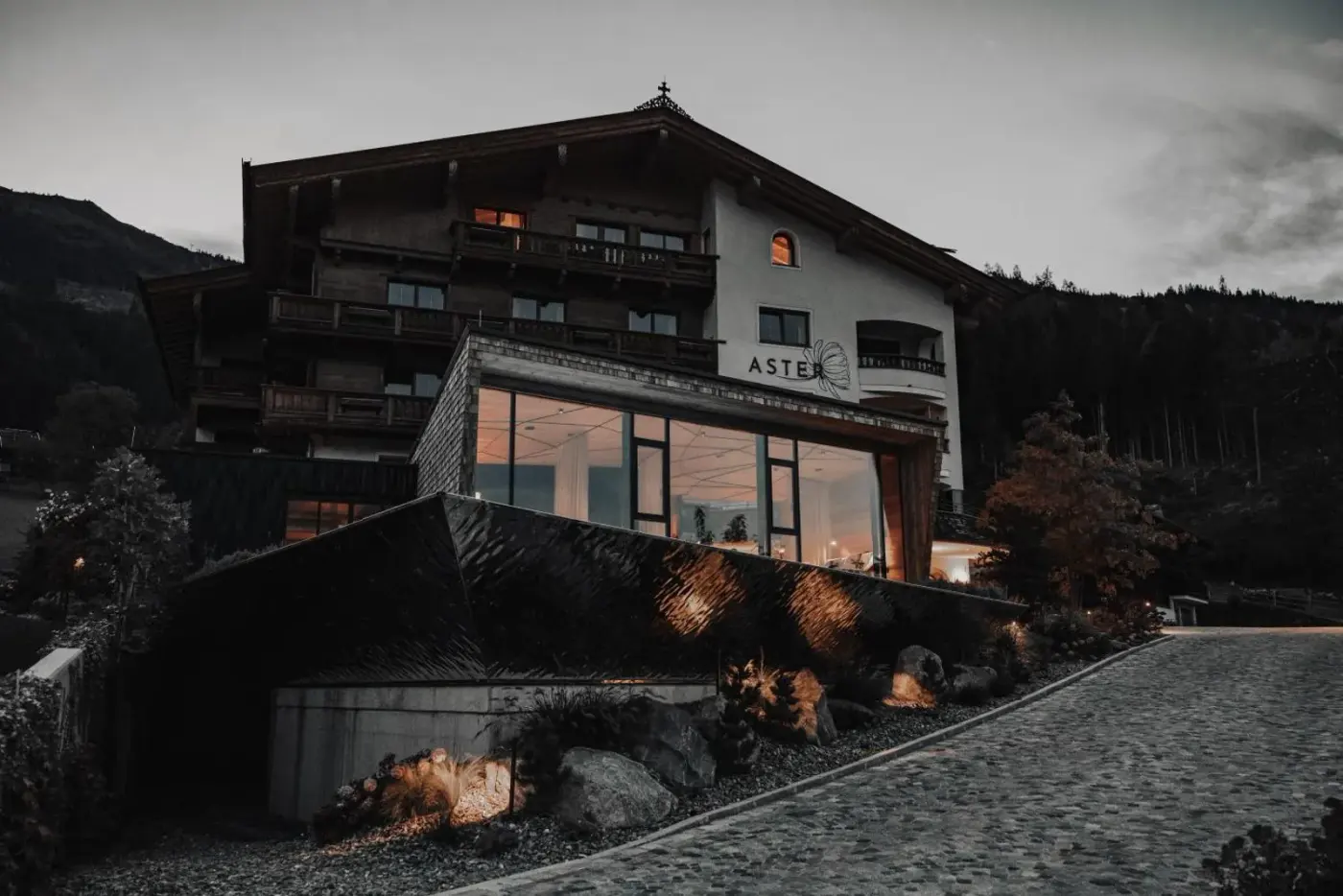 Alpine hotel building with broad spa windows at dusk at ASTER Boutique Hotel and Chalets in Fügenberg, Austria.