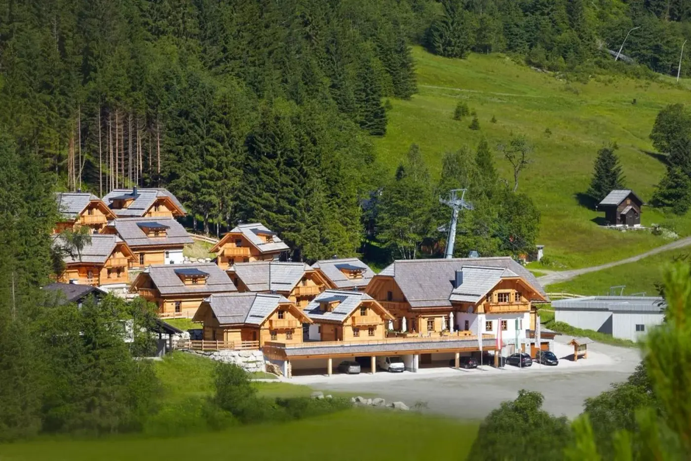 Timber chalet village on a green hillside beside a forest at Bergdorf Riesner in Irdning-Donnersbachtal, Austria.