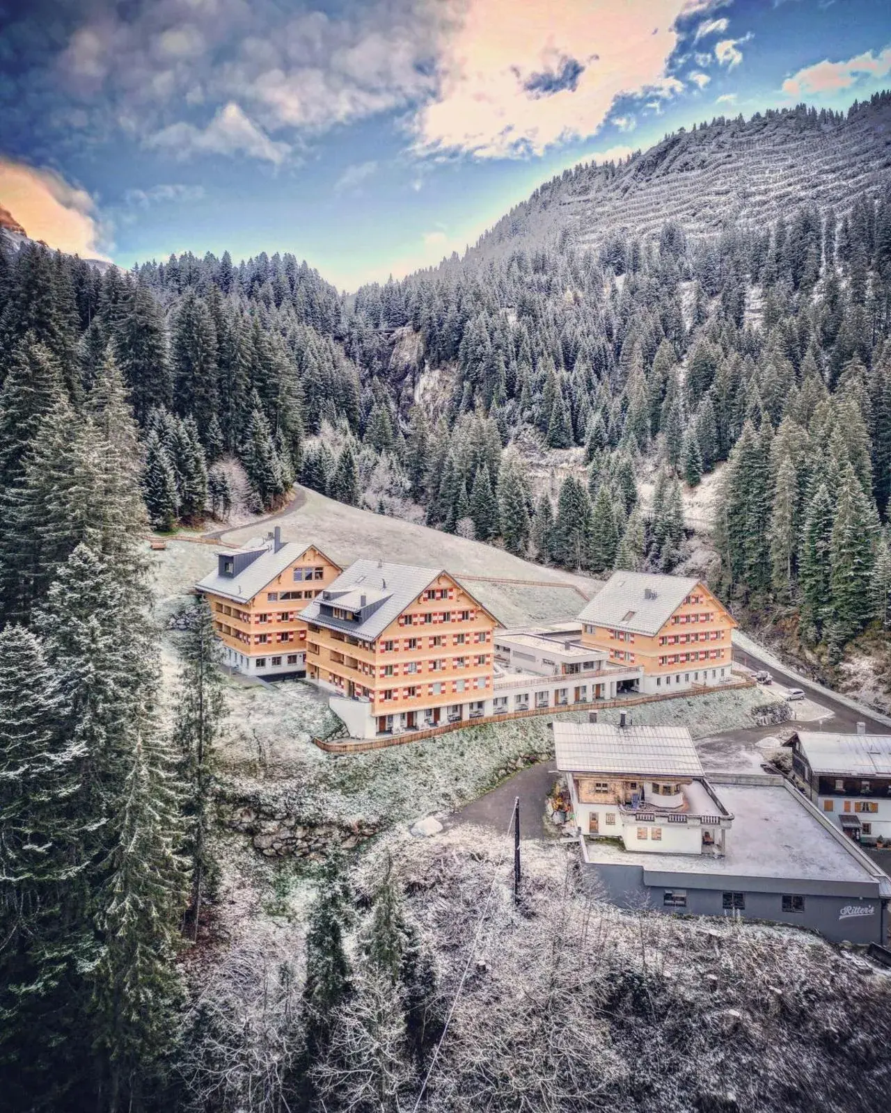 Aerial view of the alpine hotel surrounded by snow-covered forest at Berghaus Schröcken in Schröcken, Austria.