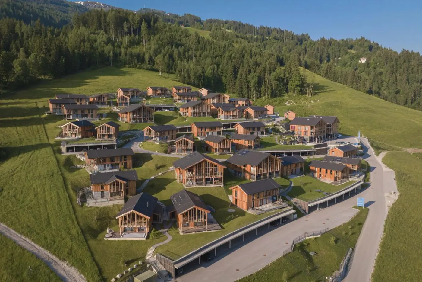 Aerial view of timber chalets on a green hillside at Bergresort Hauser Kaibling by ALPS RESORTS in Haus im Ennstal, Austria.