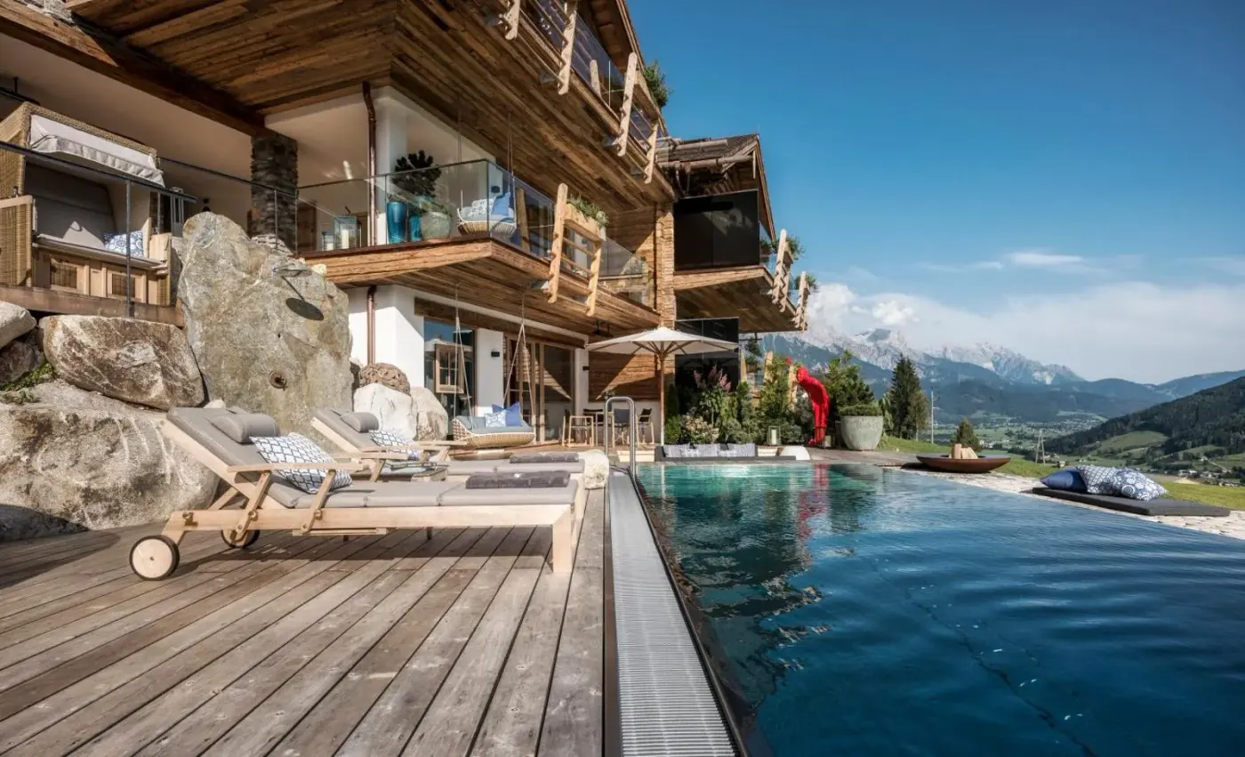 Timber chalet and pool terrace overlooking a green mountain valley at BergWärtsGeist SENHOOG in Leogang, Austria.