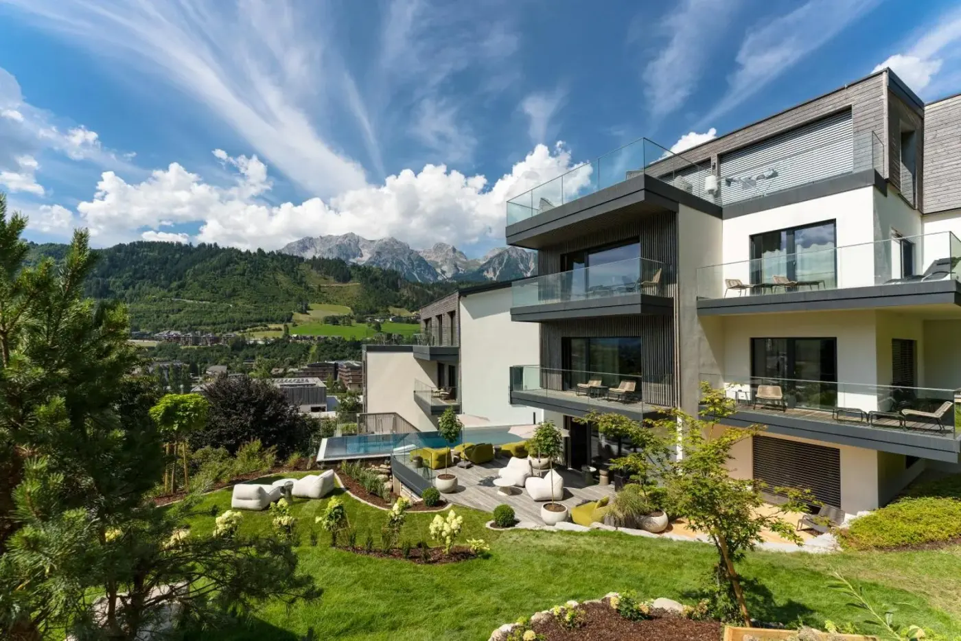 Modern aparthotel with balconies and a garden beneath mountain peaks at Chalets Coburg in Schladming, Austria.