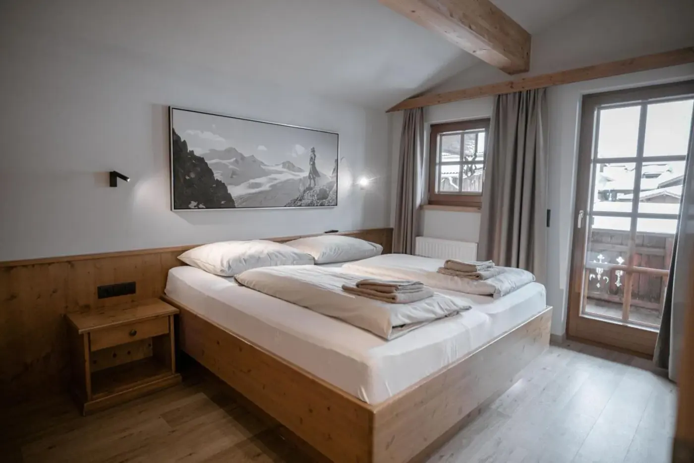 Double bedroom with timber furniture and glazed balcony doors at BRUGGER ChaletDorf in Mayrhofen, Austria.