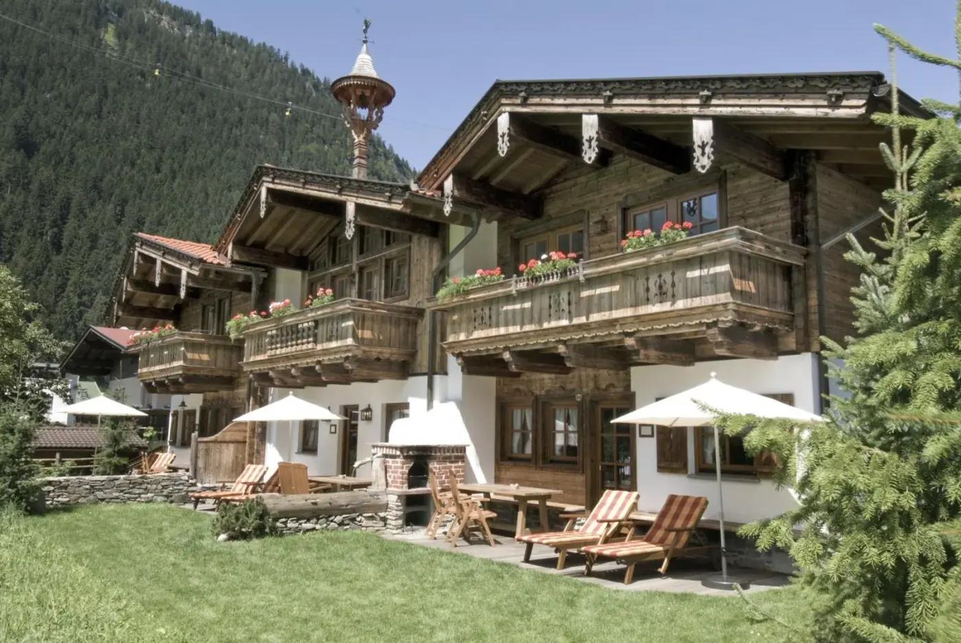 Timber chalet with flower-lined balconies and sun loungers in a garden at BRUGGER ChaletDorf in Mayrhofen, Austria.