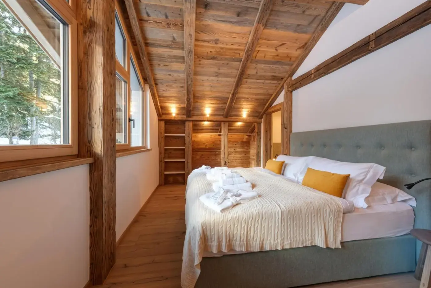 Double bedroom with exposed beams, timber flooring and large windows at Chalet Marmotta CULM in Sankt Anton am Arlberg, Austria.