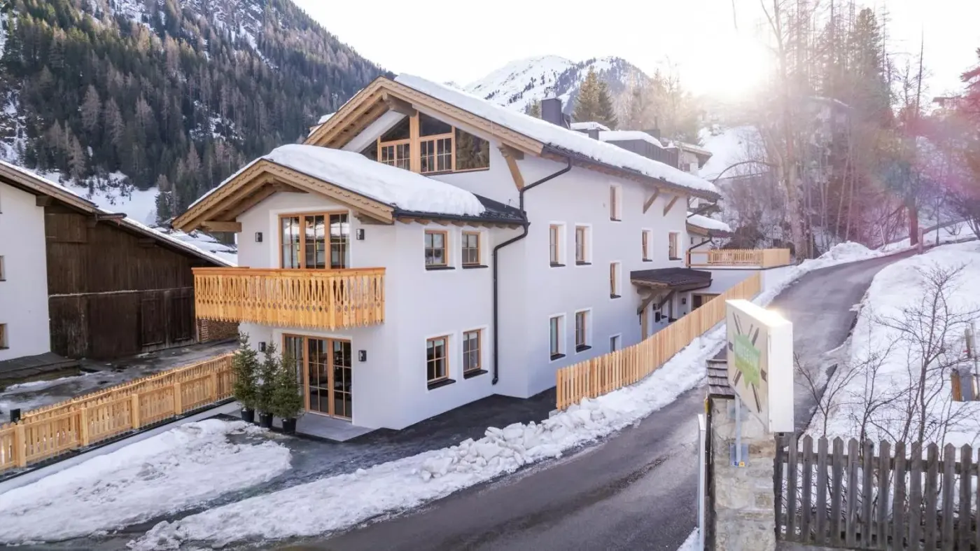 White and timber chalet exterior beside a snow-covered road at Chalet Marmotta CULM in Sankt Anton am Arlberg, Austria.