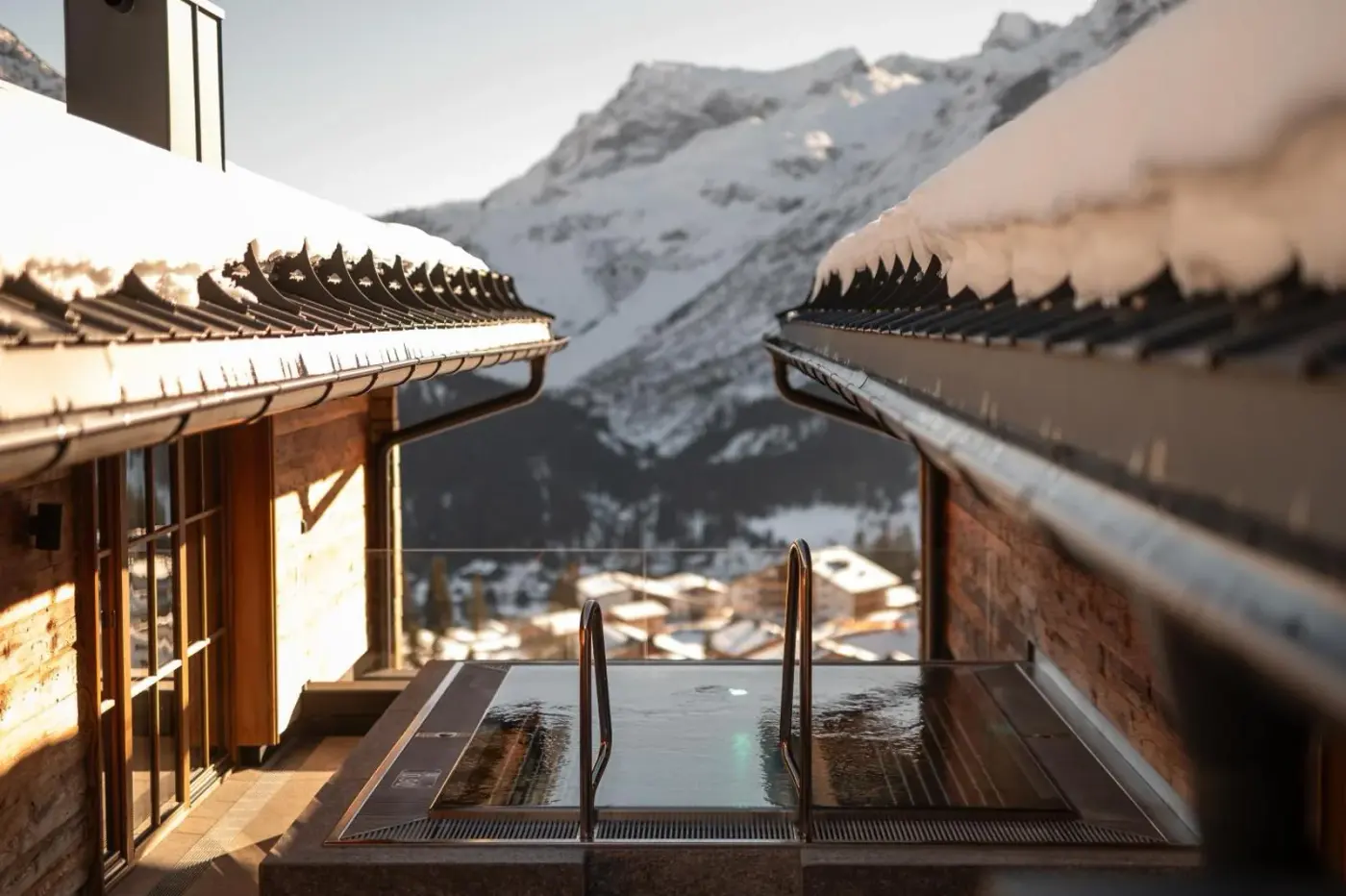 Swimming pool between chalet terraces with snowy mountains beyond at Chalet Mimi in Lech am Arlberg, Austria.