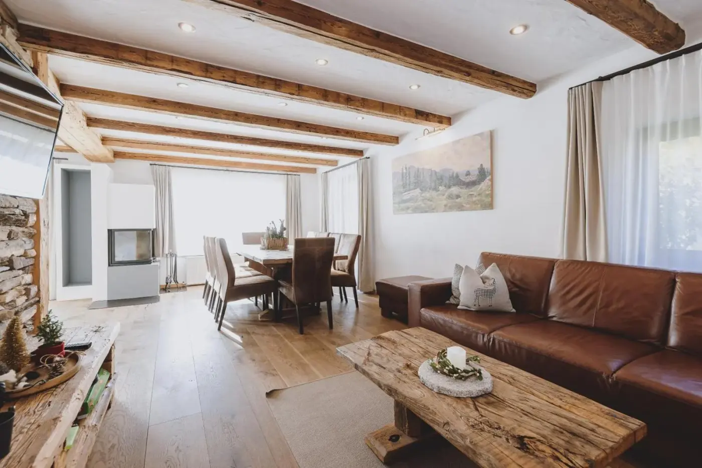 Living and dining room with a leather sofa beneath timber ceiling beams at Chalet Molly by we rent in Zell am See, Austria.