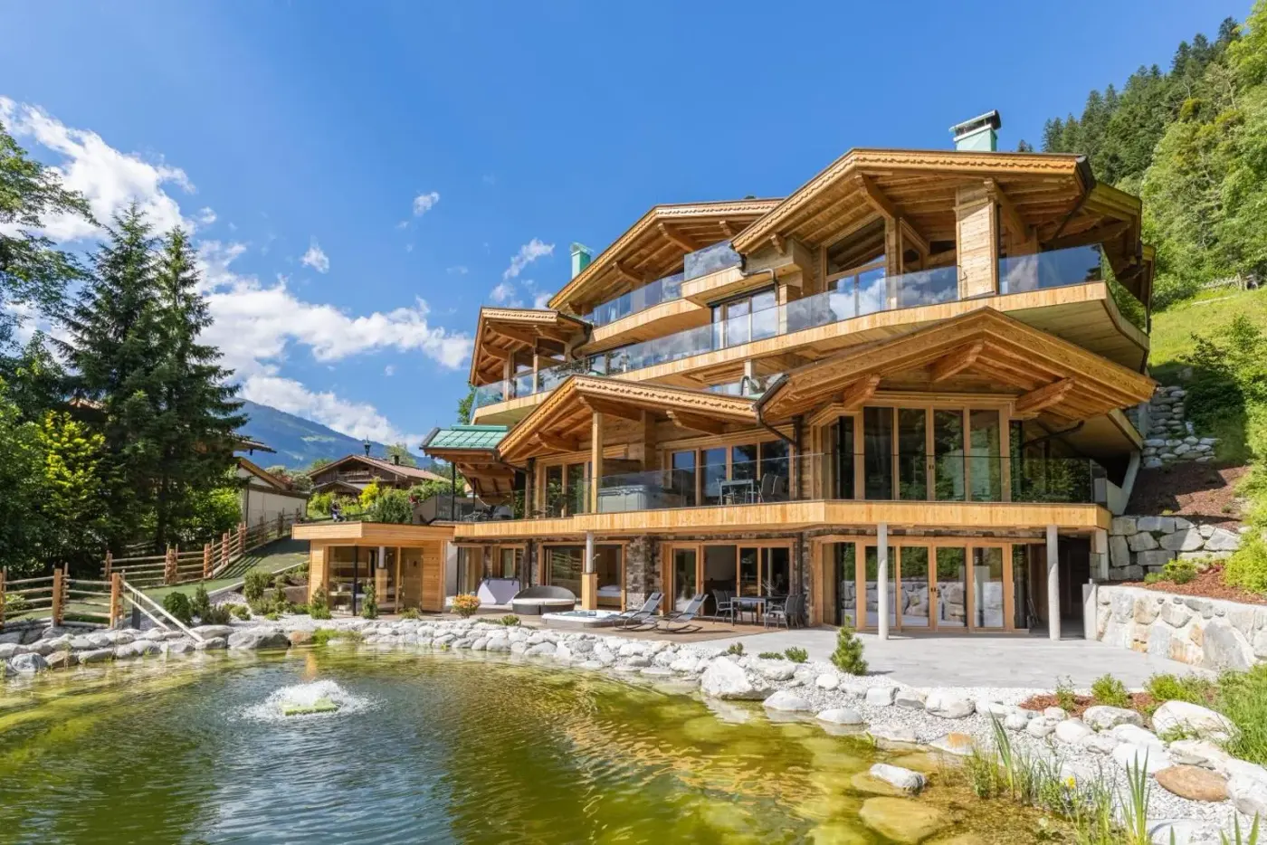 Timber chalet with broad balconies beside a landscaped garden pond at Chalet Residenz Zillertal Mühlermoos in Ramsau im Zillertal, Austria.