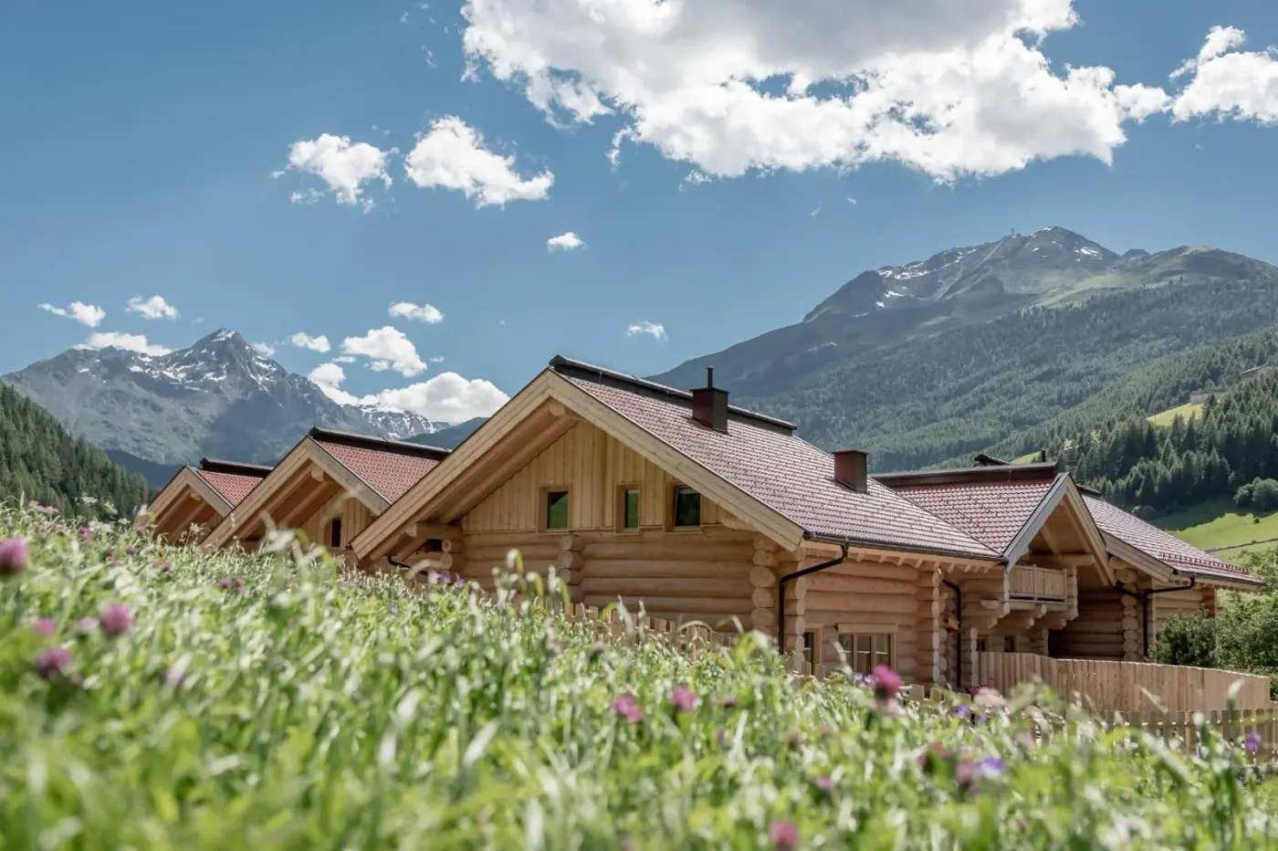 Log chalet exteriors beside a flowering meadow and alpine mountains at Chalet Resort Sölden in Sölden, Austria.
