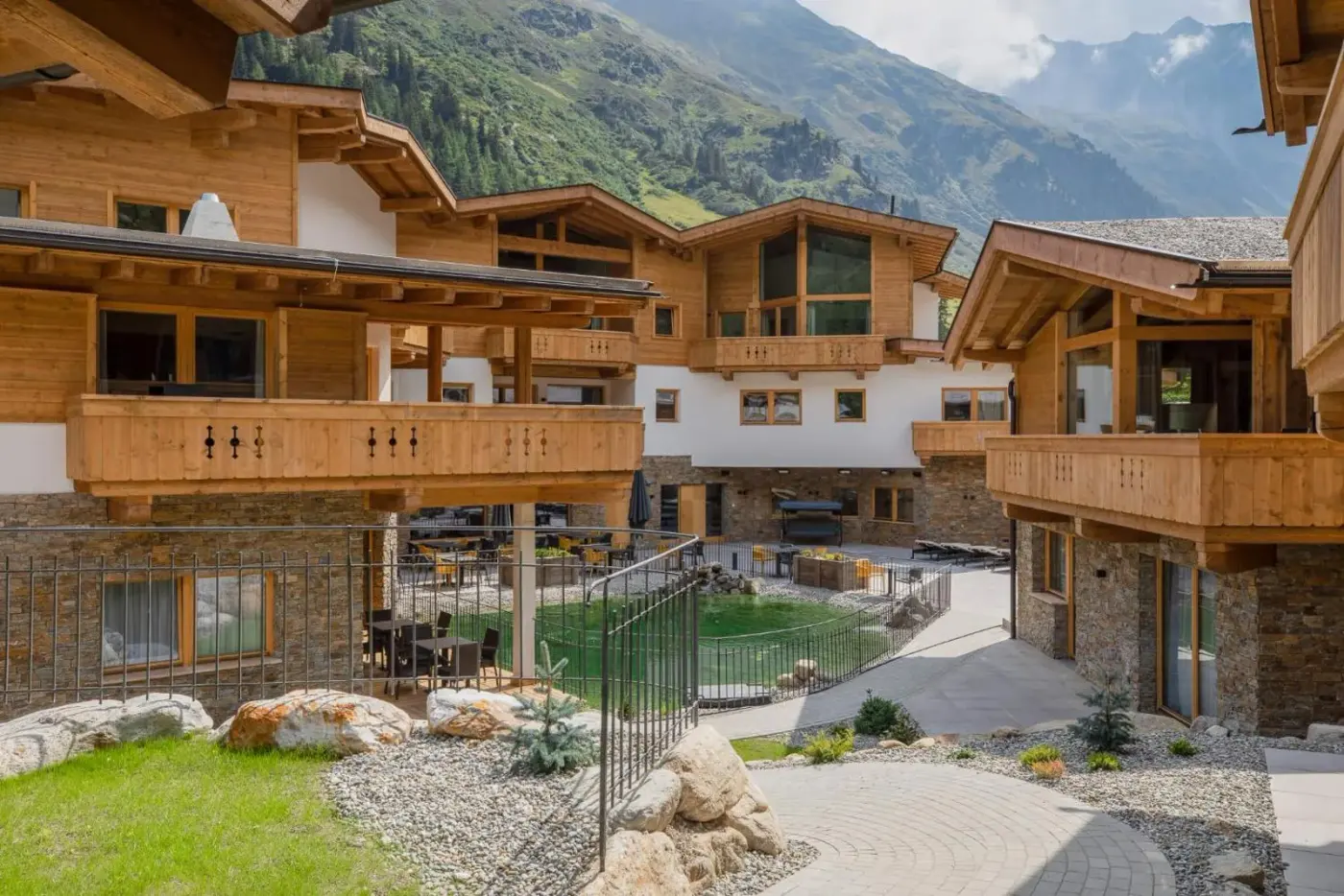 Timber-and-stone chalet village beneath green mountain slopes at das Chaletdorf Pitztal in Sankt Leonhard im Pitztal, Austria.