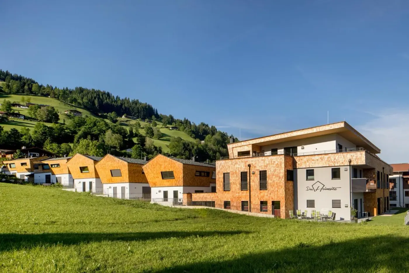 Timber-clad apartment building and chalets beside a green hillside at Das Heimsitz in Brixen im Thale, Austria.