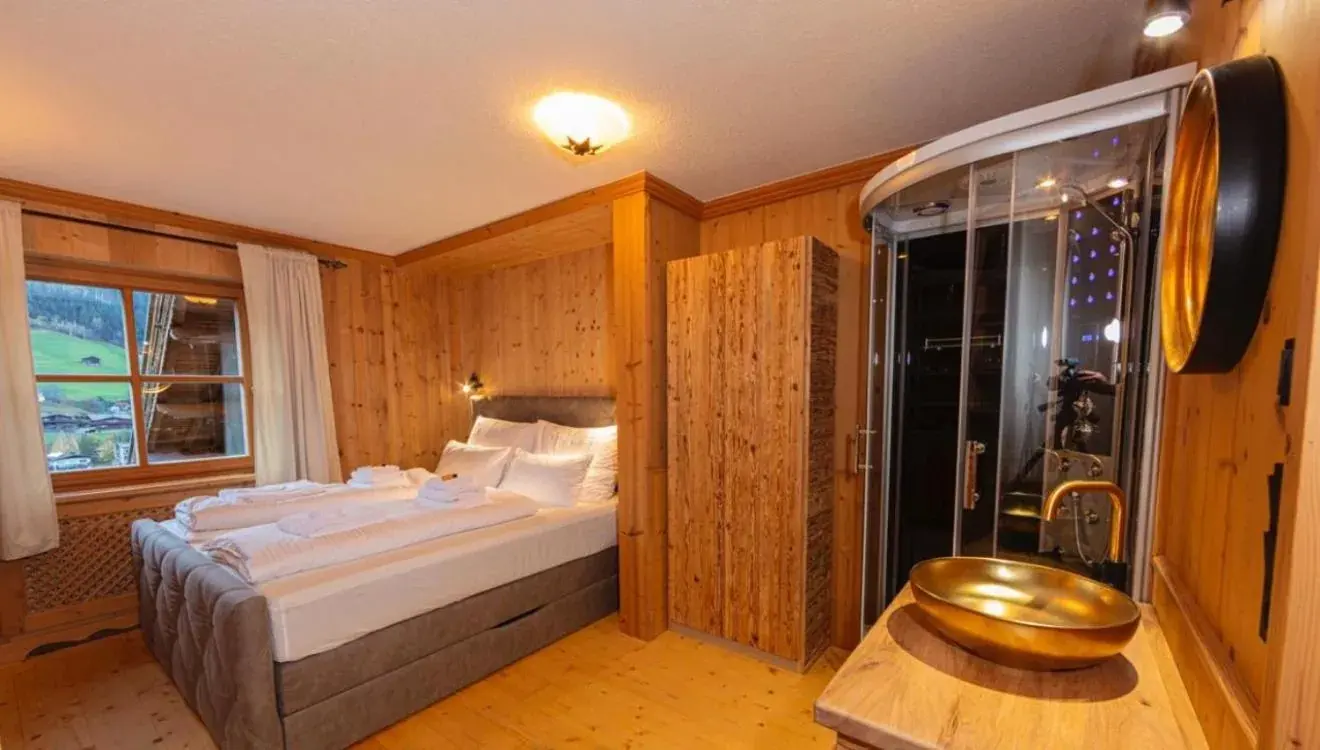 Double bedroom with timber walls and a glass-fronted shower at Das Kitz ChaletApartments in Jochberg, Austria.