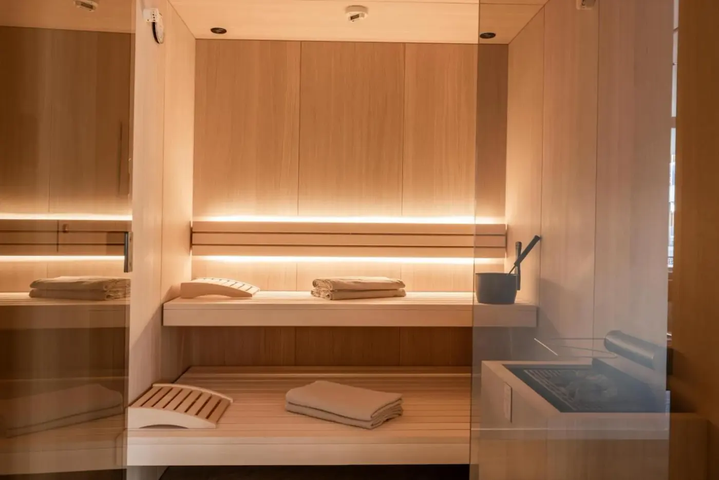 Timber-lined sauna with illuminated benches behind a glass front at Domenigs Luxury Apartments in Fiss, Austria.
