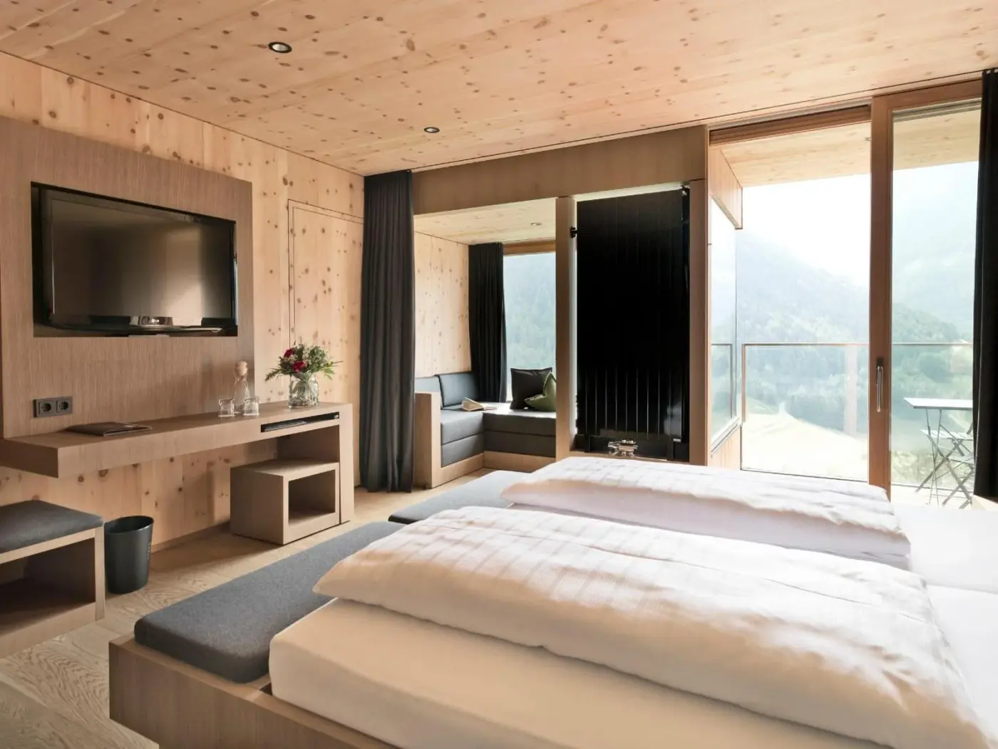 Double bedroom with timber wall panels and a panoramic window at Gradonna Mountain Resort Chalets and Hotel in Kals am Großglockner, Austria.