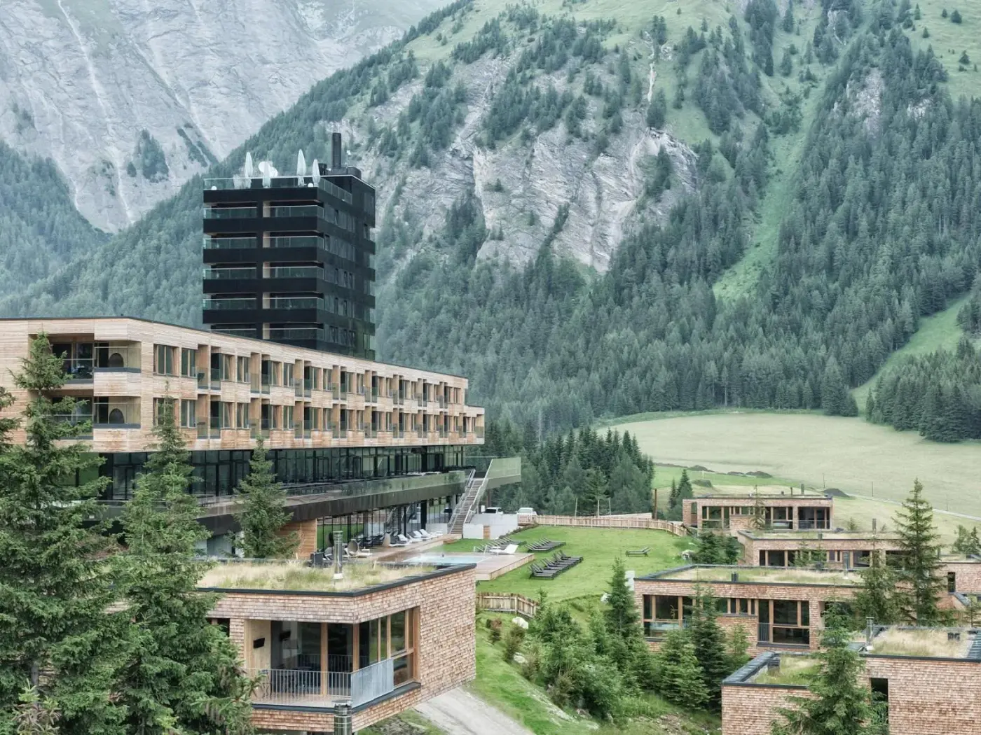 Timber mountain resort buildings beneath steep forested alpine slopes at Gradonna Mountain Resort Chalets and Hotel in Kals am Großglockner, Austria.