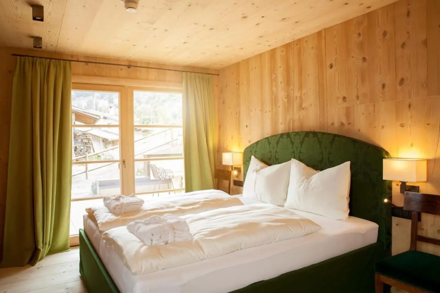 Double bedroom with pale timber walls and glazed balcony doors at HochLeger in Aschau im Zillertal, Austria.