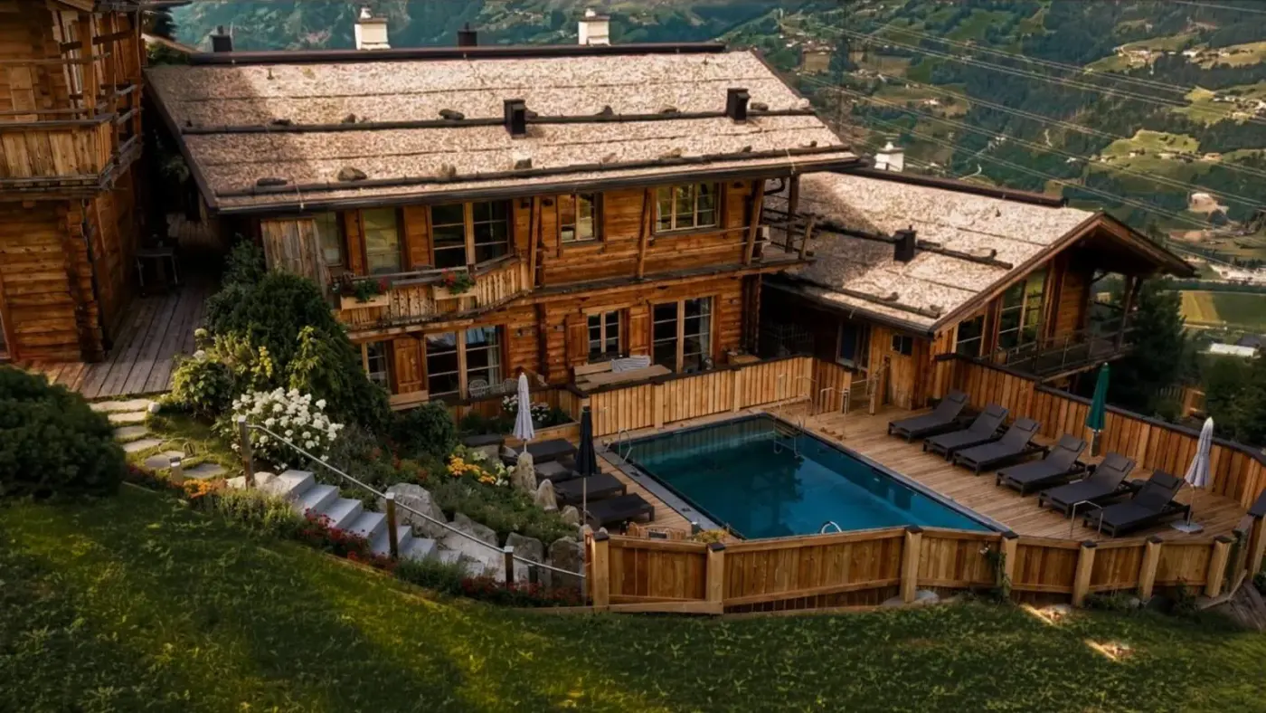 Timber chalets and an outdoor pool on a green hillside at HochLeger in Aschau im Zillertal, Austria.