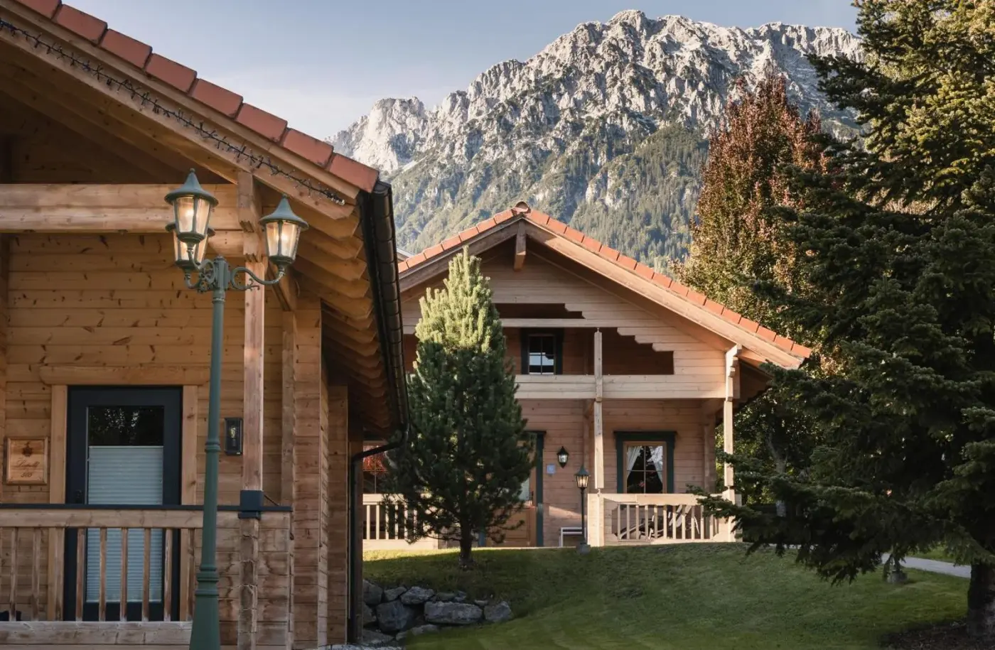 Timber chalets in a garden beneath rocky mountain peaks at Hotel Leitenhof in Scheffau am Wilden Kaiser, Austria.