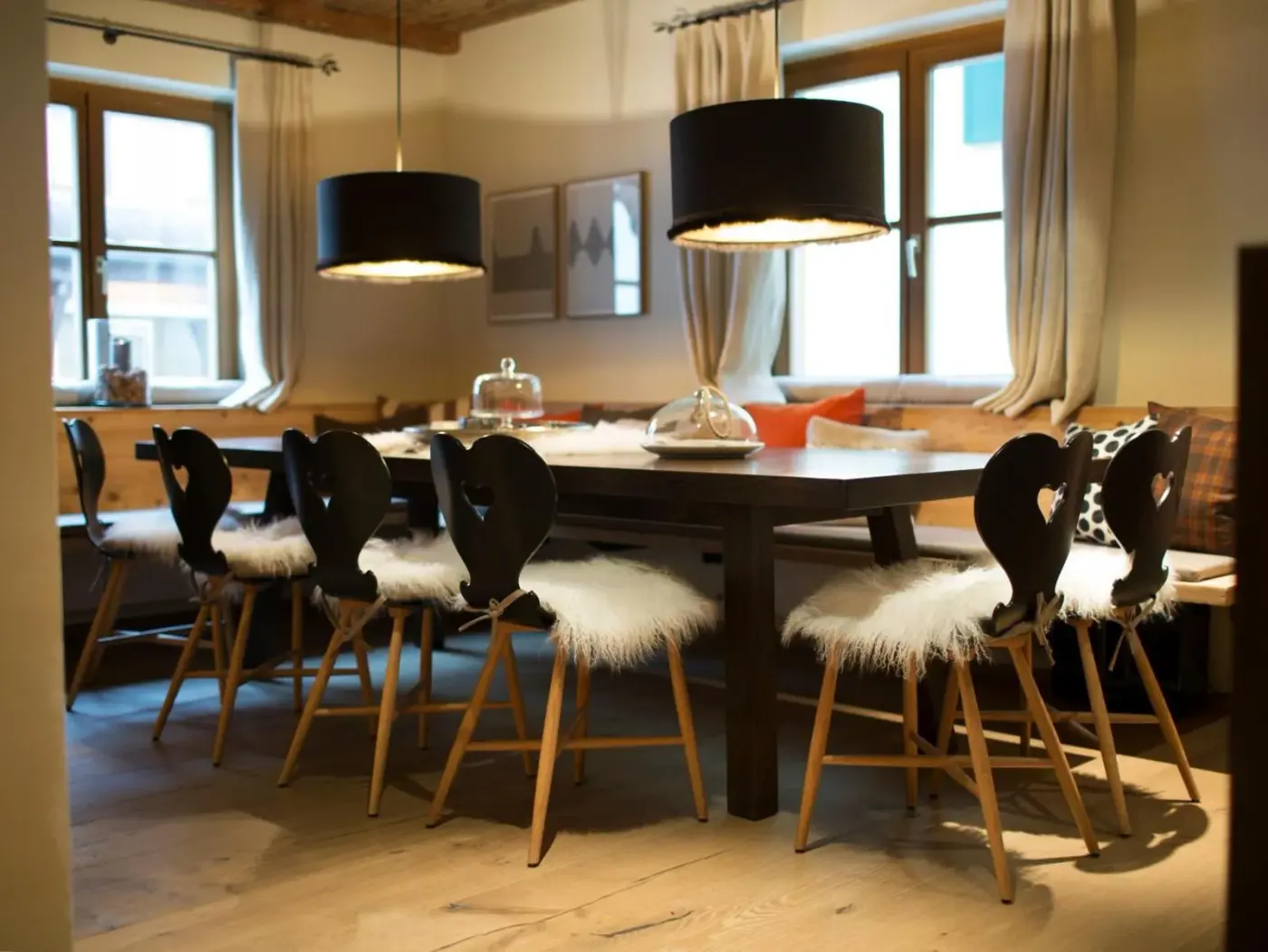 Dining room with a long wooden table, fur-covered chairs and pendant lights at House Hannes Schneider Stuben in Stuben am Arlberg, Austria.