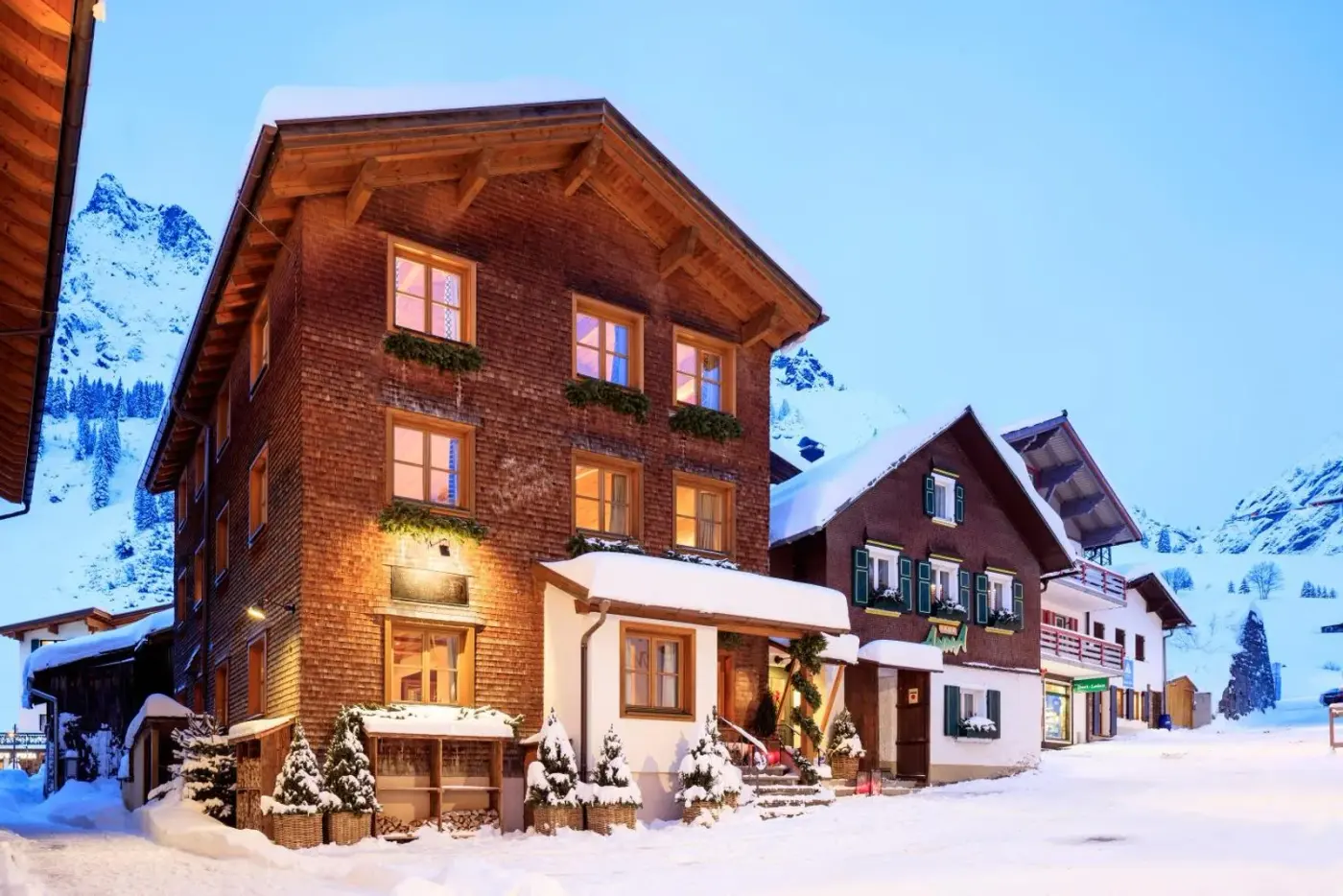 Illuminated timber chalet exterior in a snow-covered alpine village at House Hannes Schneider Stuben in Stuben am Arlberg, Austria.