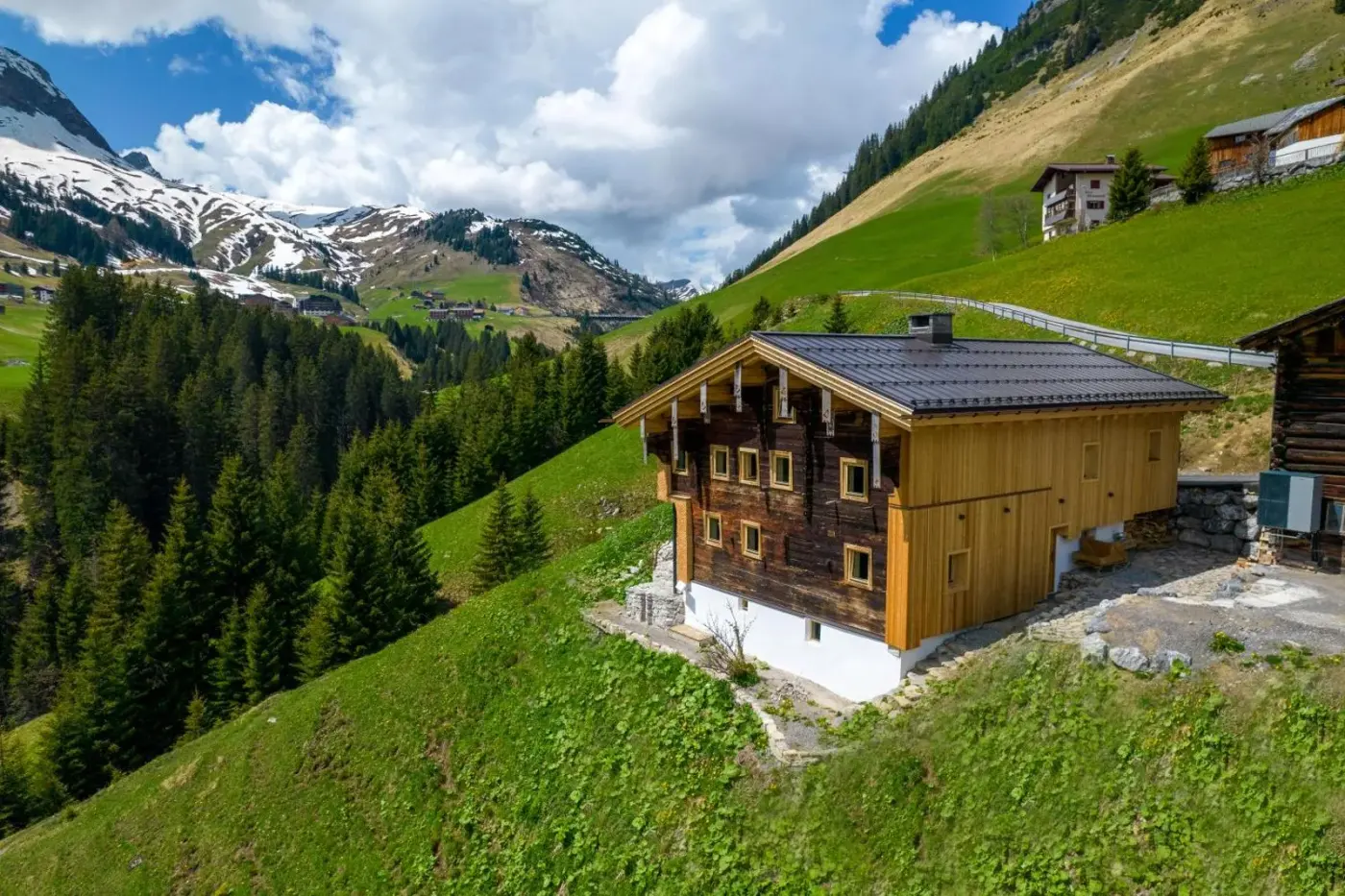 Timber chalet on a green alpine hillside beneath rocky mountains at Jup Boutique Chalet in Warth am Arlberg, Austria.