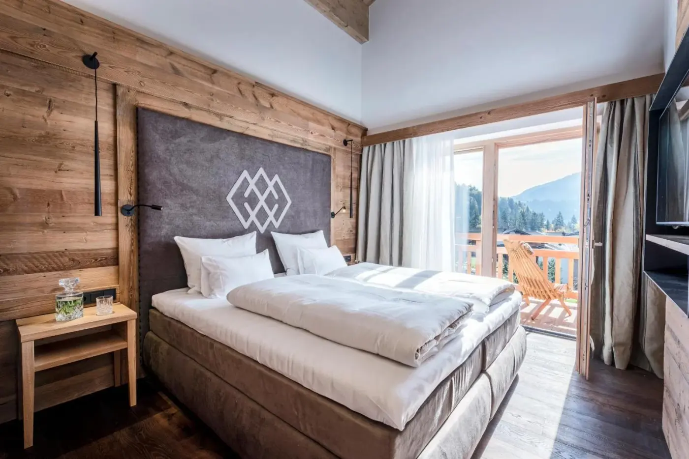 Double bedroom with a timber feature wall and glazed balcony doors at Kaiserlodge in Scheffau am Wilden Kaiser, Austria.