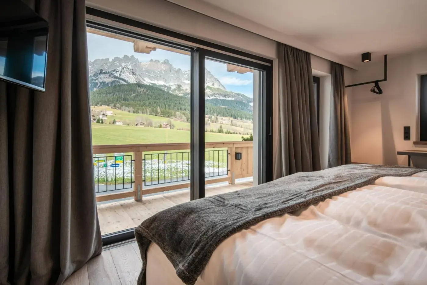 Double bedroom with glazed balcony doors overlooking fields and mountains at KaiserMoments in Going am Wilden Kaiser, Austria.