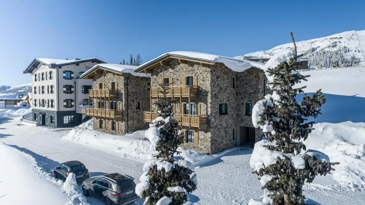Stone chalet exteriors with timber balconies surrounded by snow at KAUZ Design Chalets in St. Michael im Lungau, Austria.