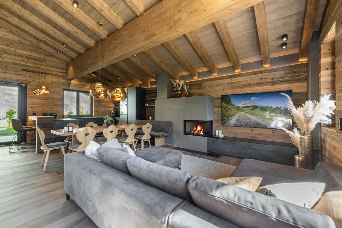 Living and dining room with a grey sofa, timber ceiling and fireplace at Kellnergut Chalet Frieda in Mühlbach am Hochkönig, Austria.
