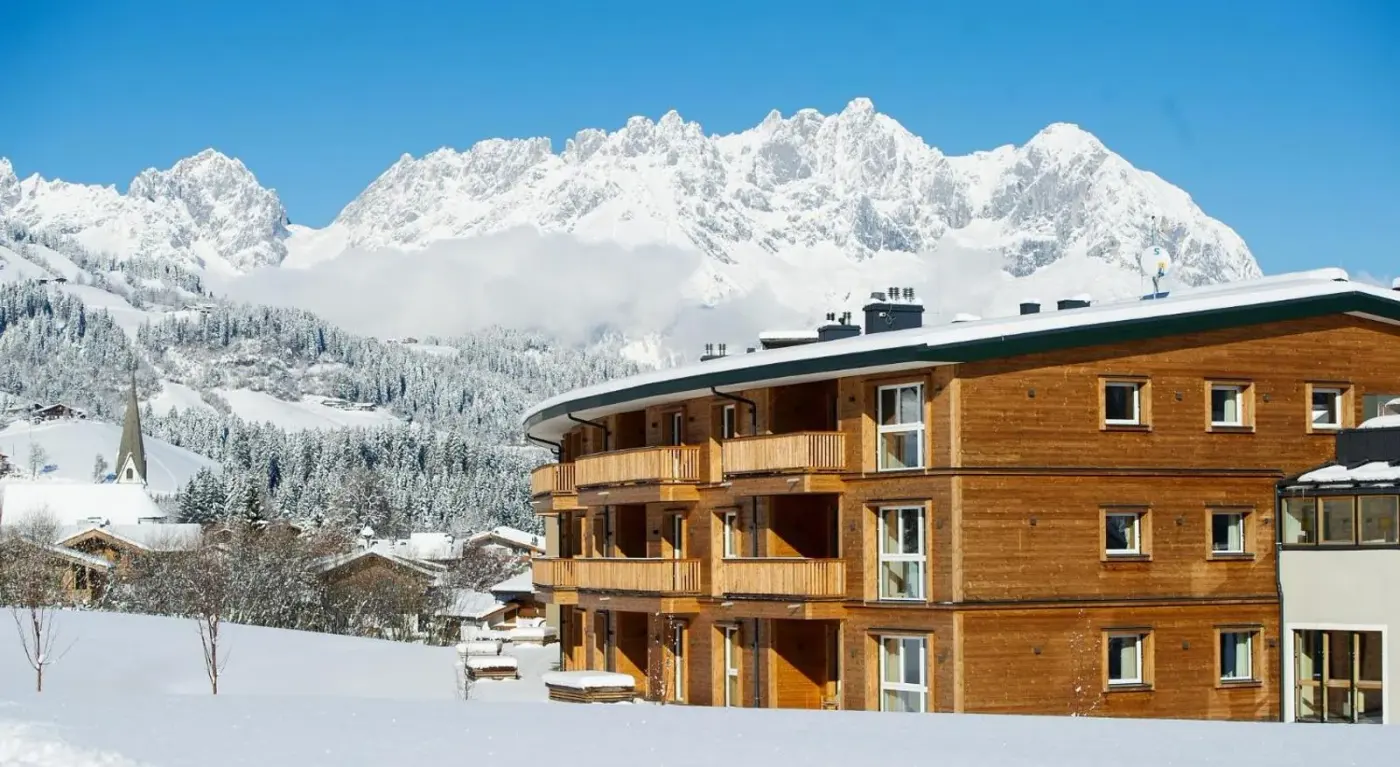 Timber lodge exterior beneath snow-covered mountain peaks at Kitzbühel Lodge in Reith bei Kitzbühel, Austria.