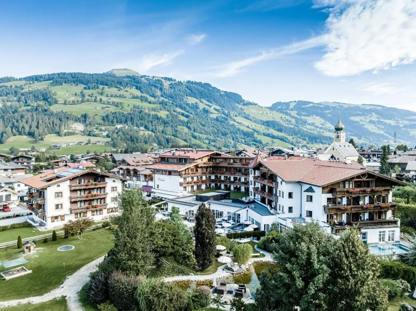 Hotel and gardens in an Alpine village beneath green mountain slopes at Landhotel Schermer in Westendorf, Austria.