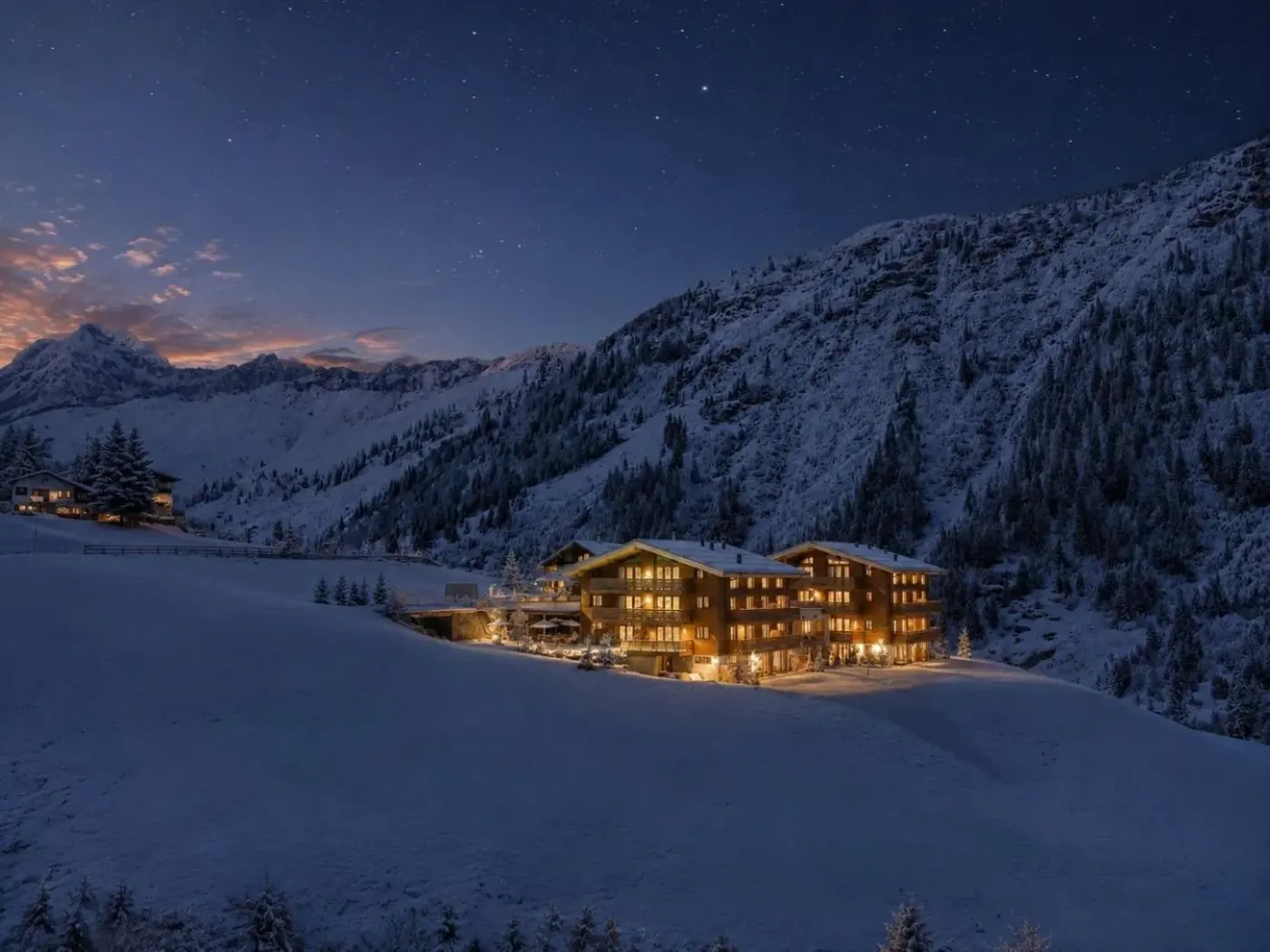 Illuminated timber chalet surrounded by snowy mountains at dusk at LUX ALP CHALET in Warth am Arlberg, Austria.