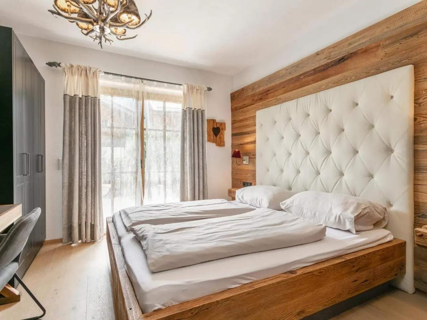 Double bedroom with a tall padded headboard and glazed terrace doors at Maier Alm in Neukirchen am Großvenediger, Austria.