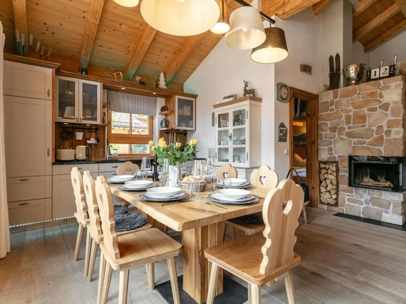 Kitchen and dining room with a stone fireplace and carved wooden chairs at Maier Alm in Neukirchen am Großvenediger, Austria.