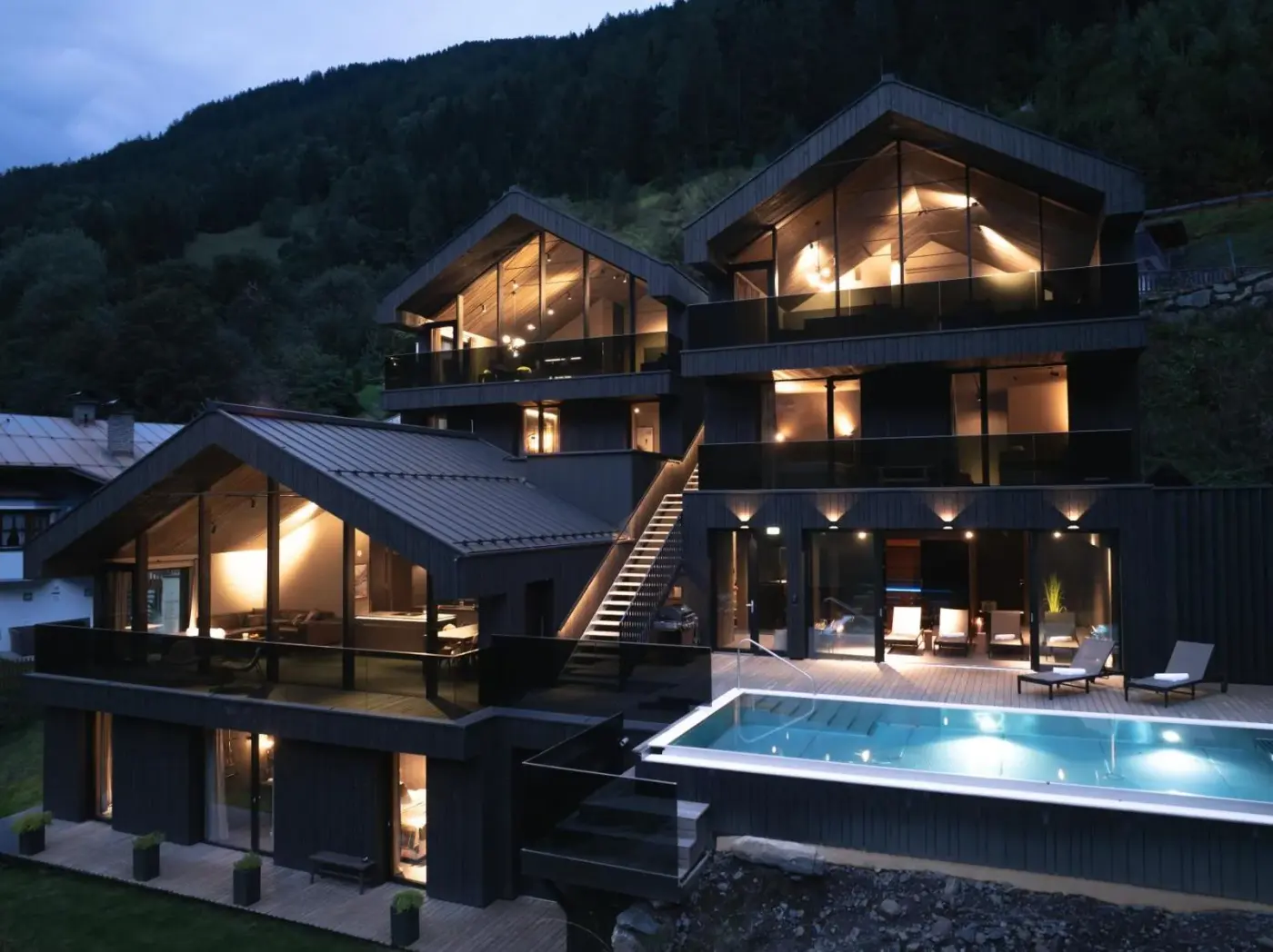 Illuminated timber-clad villas and an outdoor pool at dusk at Paznauner Villen in Kappl, Austria.