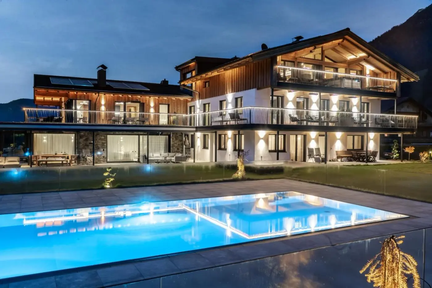 Illuminated chalet exterior beside an outdoor swimming pool at Purest in Achenkirch am Achensee, Austria.