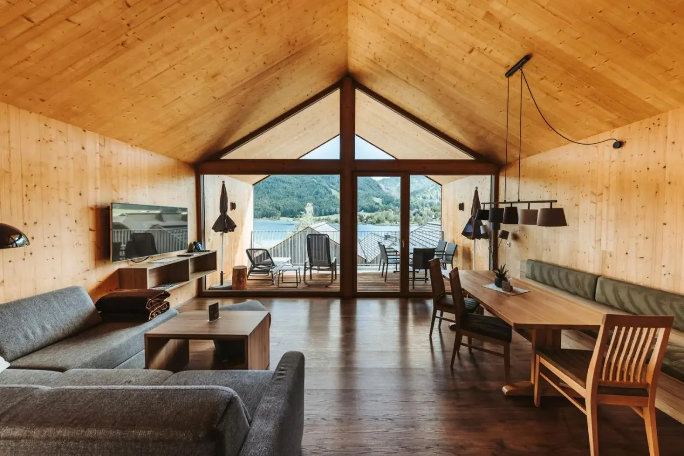 Loft living room with sofas, a timber ceiling and lake-facing balcony doors at Regitnig Hotel and Chalets in Weissensee, Austria.