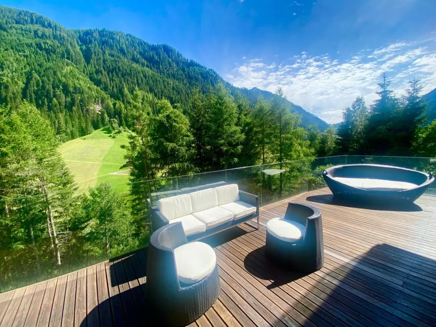 Terrace with lounge furniture and a round outdoor tub overlooking alpine forest at Schooren des Alpes in Kappl, Austria.